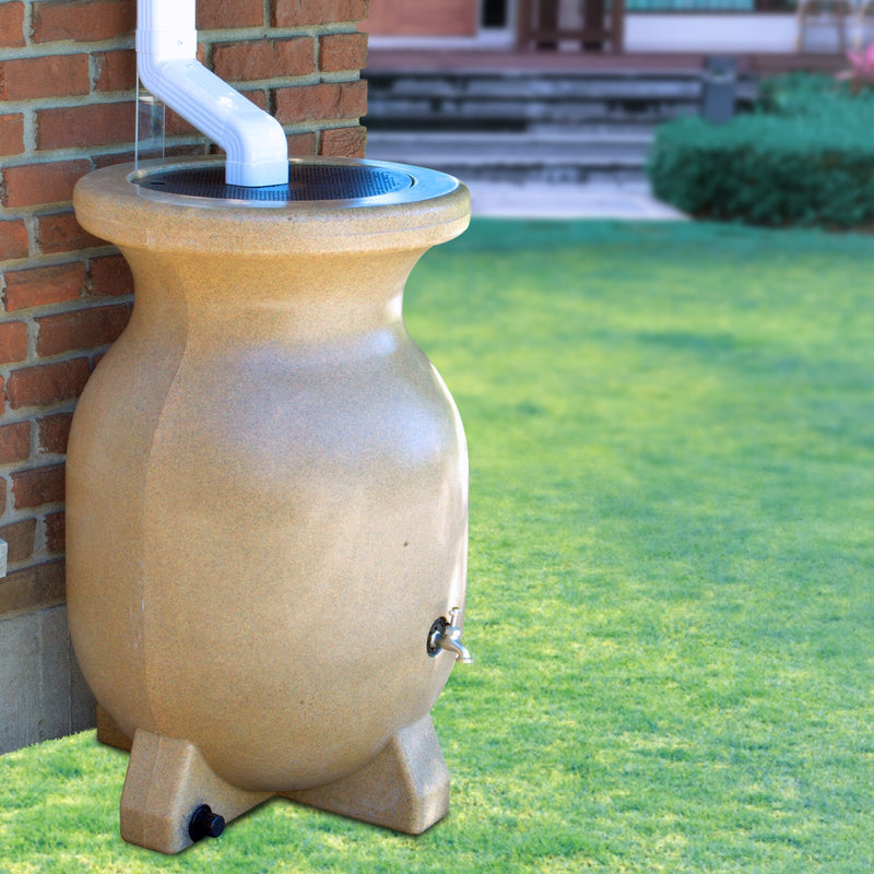Koolscapes rain barrel set up below a white downspout with a red brick wall and a garden in the background